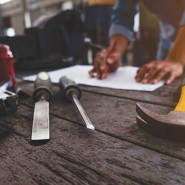 Vintage tone of equipment on wooden desk with man working in workshop background. Retro filter effect, low light.